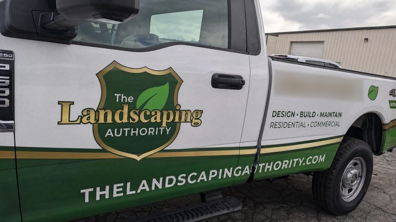 Concept mockup close-up: driver door of a white pickup with a green shield and leaf logo, gold "Landscaping" lettering, and the website on the green lower band.