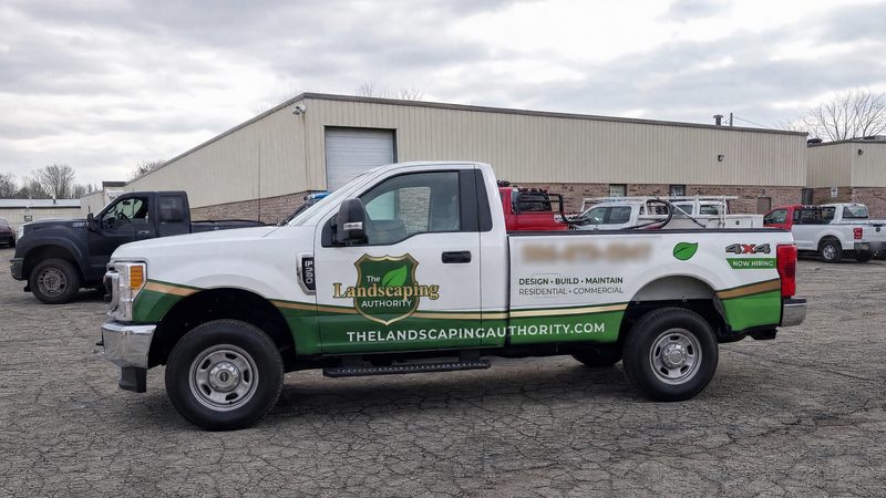 Concept mockup: white Ford F-250 pickup, driver-side profile in front of a warehouse, showing the green lower band with a gold stripe, the shield door logo, and "Design · Build · Maintain" text on the bed side.