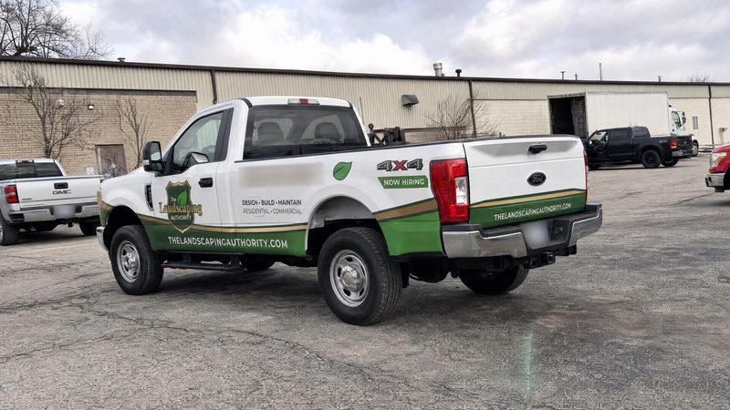 Concept mockup: white Ford F-250 pickup, rear three-quarter view, with the green band and gold stripe continuing across the tailgate and the website printed on it.